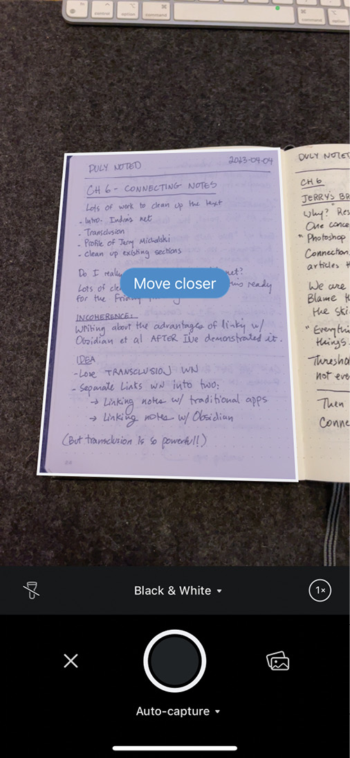 Scanner Pro应用中的iPhone相机视图显示笔记本页面。应用已检测到笔记本页面的边缘，屏幕中心的蓝色气泡显示”靠近一点”。